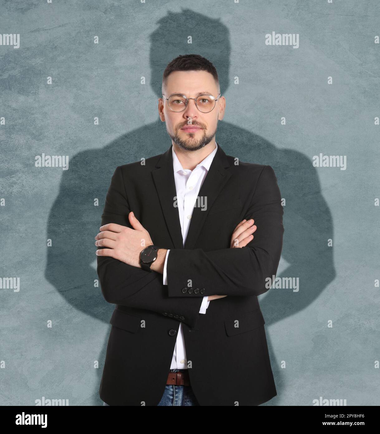 Uomo d'affari e ombra di forte uomo muscolare dietro di lui su parete grigia. Concetto di resistenza interna Foto Stock