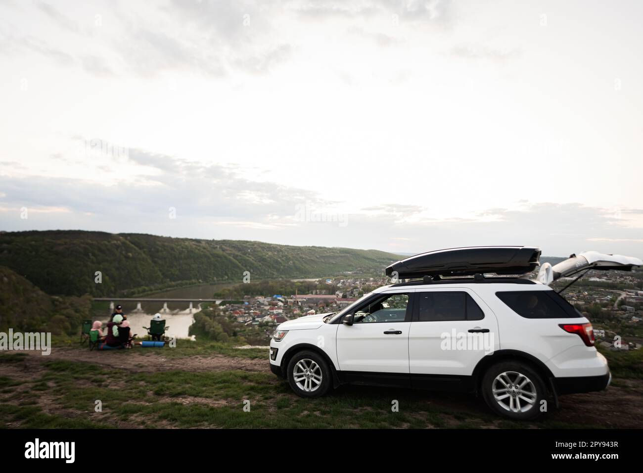 SUV auto americana con box portabagagli sul tetto contro escursioni in famiglia in vacanza, con picnic serale in cima al paesaggio del canyon di montagna. Foto Stock