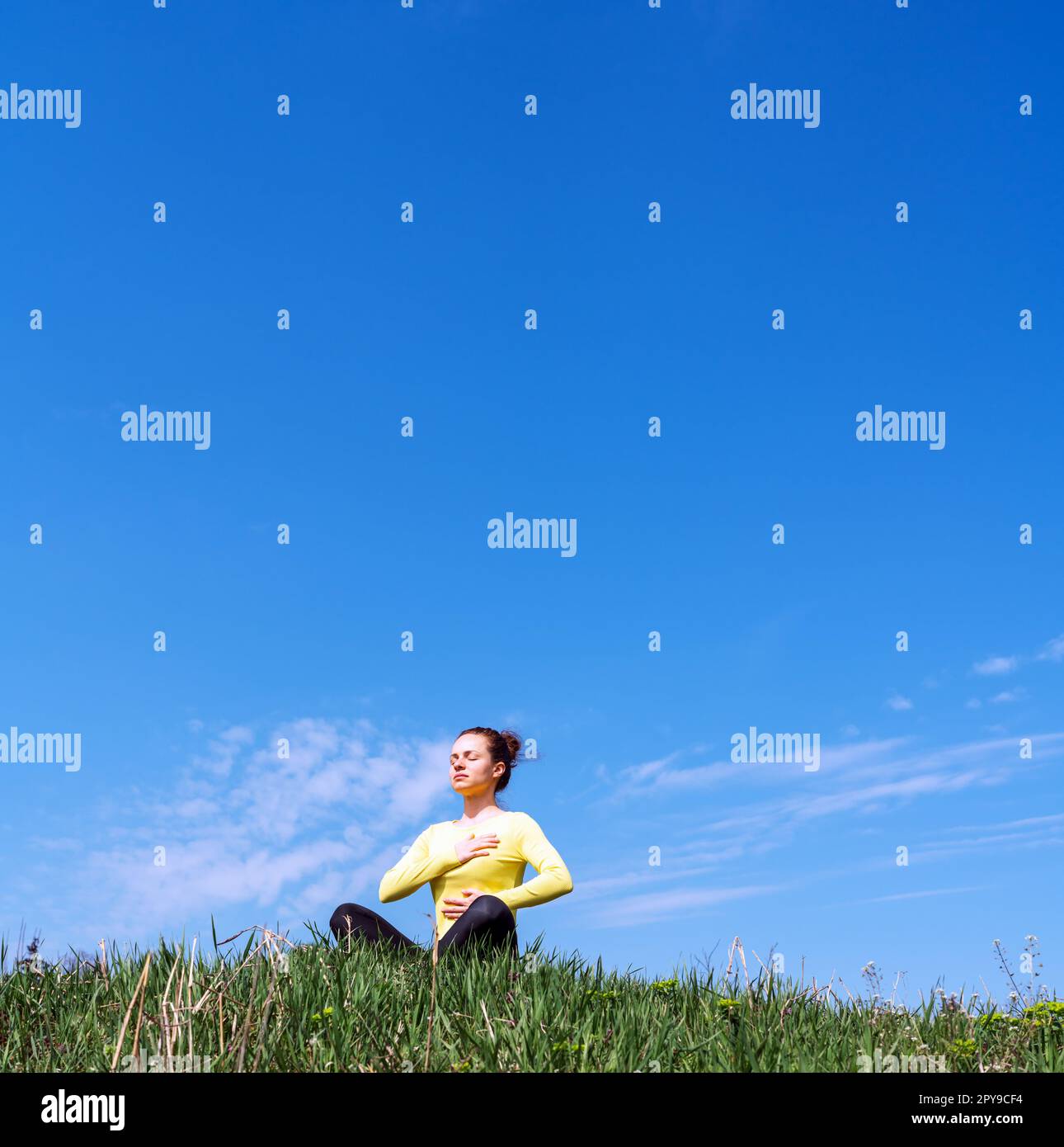 Yoga respirazione esercizio all'aperto in natura, donna meditando su erba verde contro il cielo blu. Foto Stock