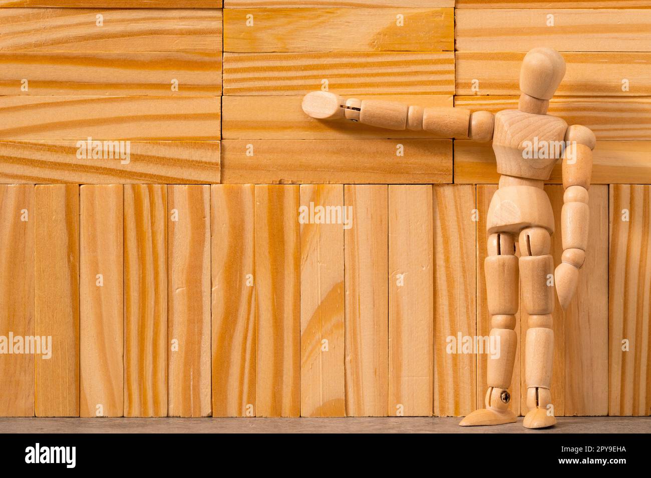 Figura uomo di legno che si trova accanto a una parete di legno fatta di blocchi di legno Foto Stock