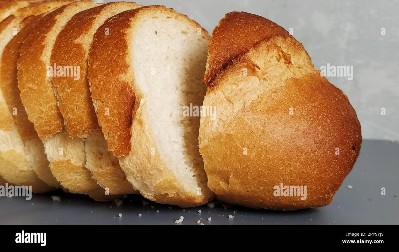 Pane affettato di farina di grano. Stuzzicanti fette di panino bianco con croccante croccante. Prodotto contenente glutine. Pane fresco. Sfondo grigio. Briciole sul tavolo. Foto Stock