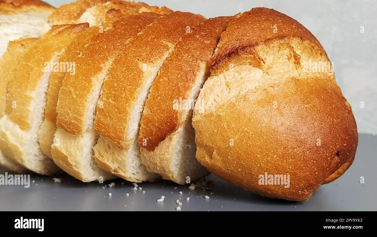 Pane affettato di farina di grano. Stuzzicanti fette di panino bianco con croccante croccante. Prodotto contenente glutine. Pane fresco. Sfondo grigio. Briciole sul tavolo. Foto Stock