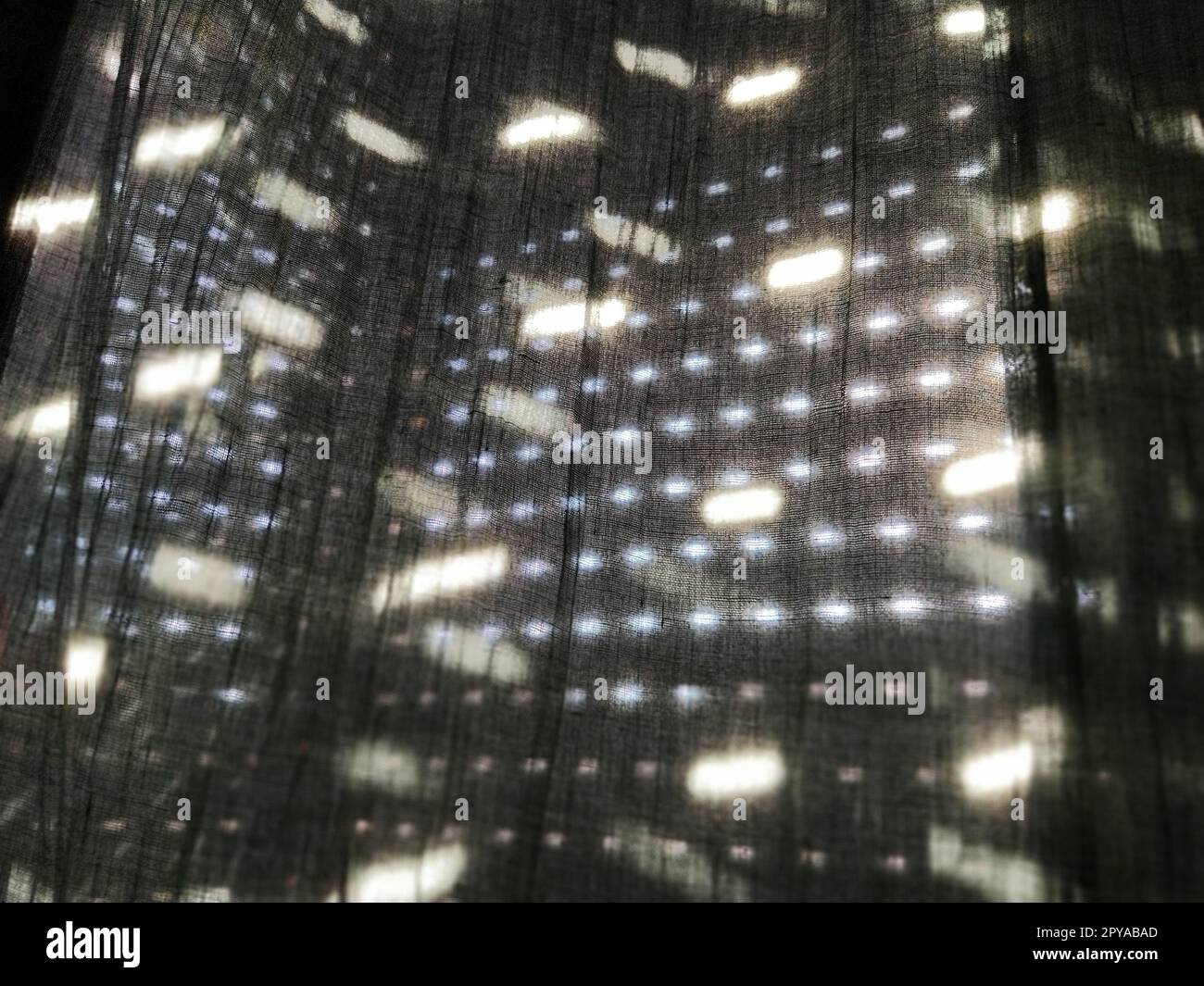 La luce del sole splende attraverso tende con piccoli fori e tende grigie - tulle. Immagine astratta. Atmosfera estiva. Riflessione dei punti luminosi sul tessuto Foto Stock