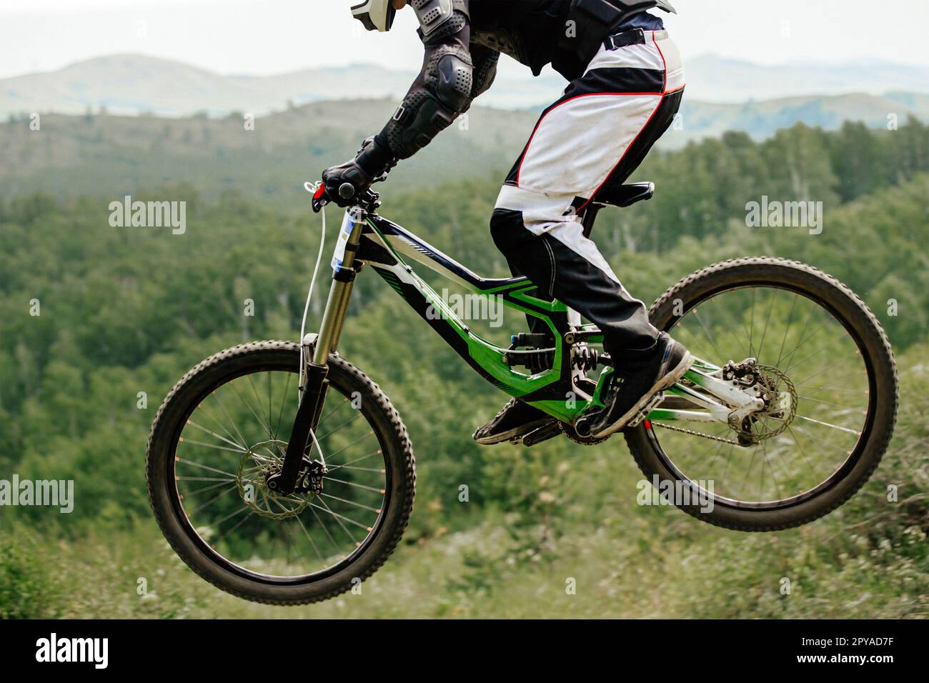 atleta ciclista discesa salto su foresta sfondo e montagne, campionato estivo di mountain bike Foto Stock