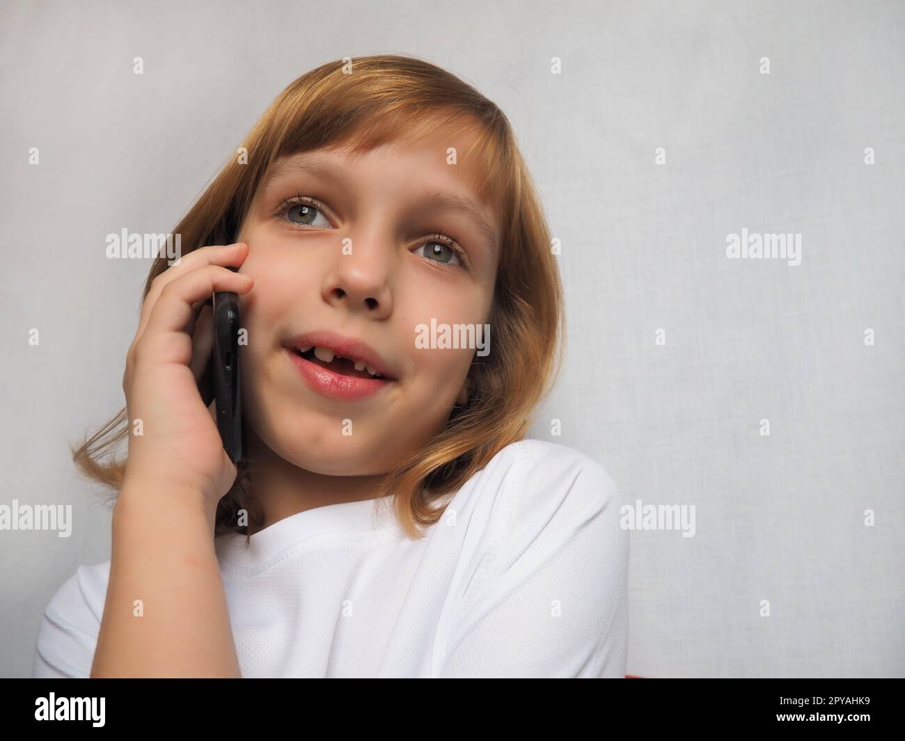 bambina di 7 anni senza dente anteriore. Il bambino sorride, guarda lontano e parla al telefono o allo smartphone. Cambio dei denti del latte nell'infanzia. Ortodonzia e studio odontoiatrico Foto Stock