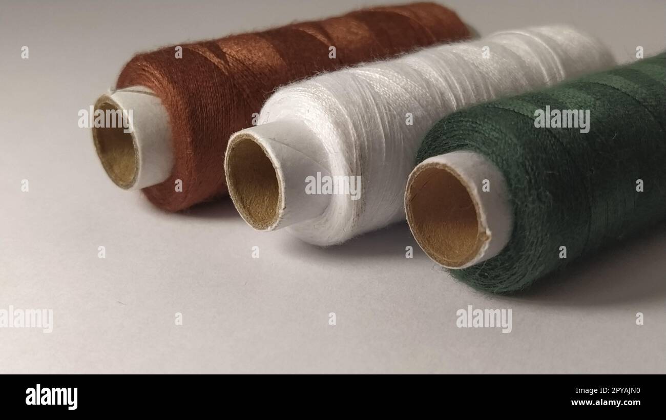 Rocche e rocchetti di filo di diversi colori - marrone, bianco e verde. Primo piano. Luce naturale sul lato sinistro. Matasse di filo. Forniture per cucire Foto Stock