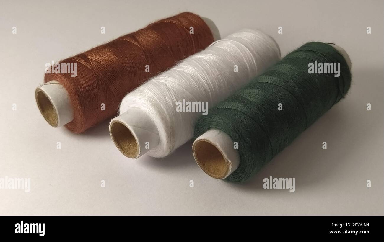 Rocche e rocchetti di filo di diversi colori - marrone, bianco e verde. Primo piano. Luce naturale sul lato sinistro. Matasse di filo. Forniture per cucire Foto Stock