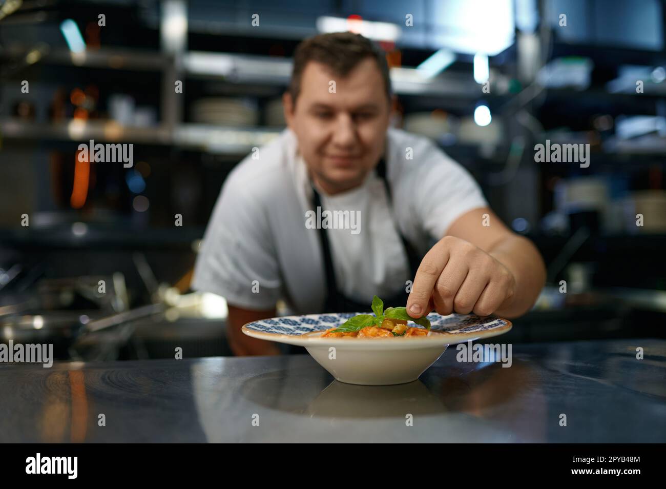Ritratto di chef soddisfatto mettendo foglia di basilico in piatto con pasta Foto Stock