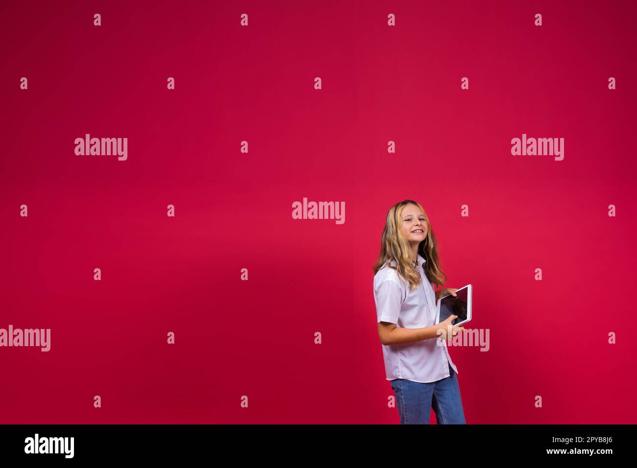 App scolastica online. Schoolgirl che mostra lo schermo vuoto del computer tablet su sfondo rosso. Studio Shot Foto Stock