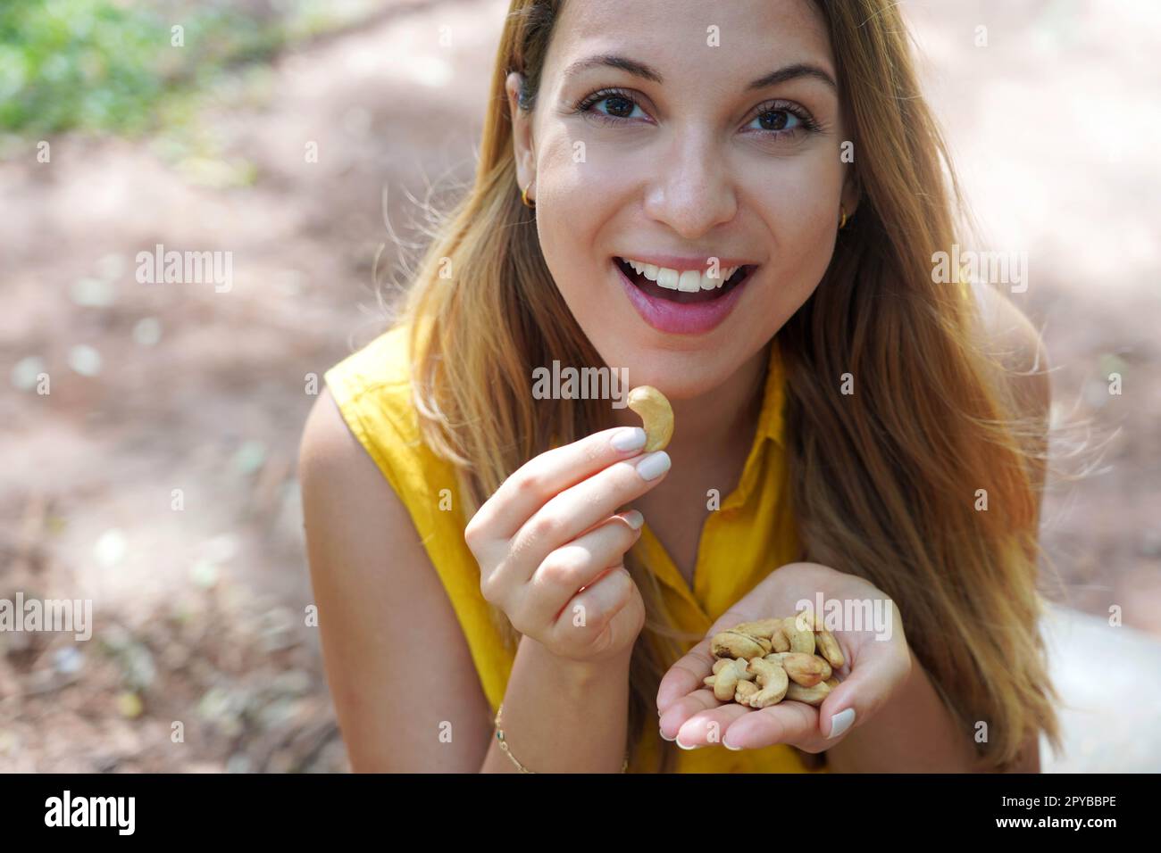 Bella ragazza sana mangiare noci anacardi nel parco. Guarda la fotocamera st. Foto Stock