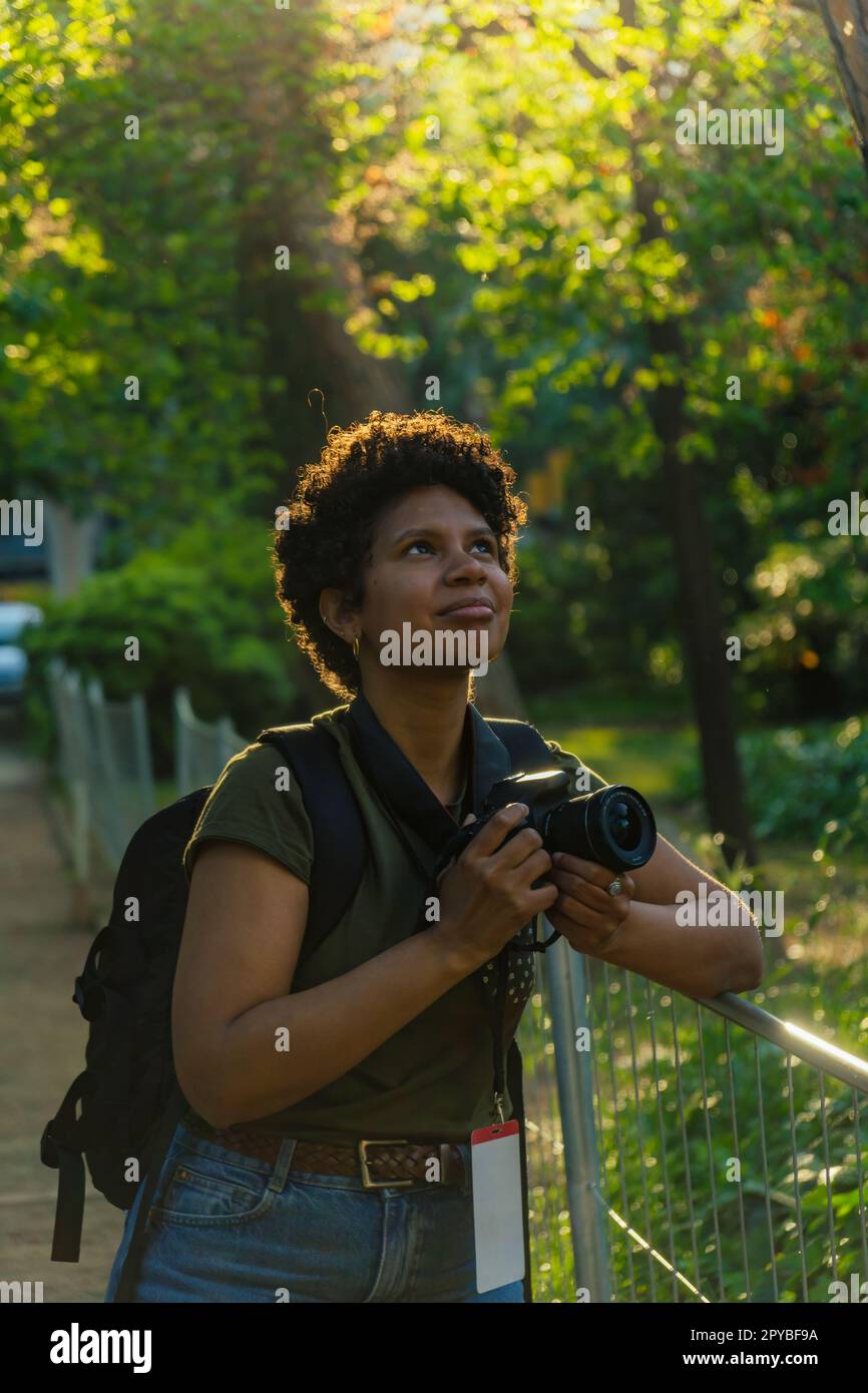 Giovane fotogiornalista nera africana americana con capelli ricci scuri alla ricerca di uccelli da fotografare con la fotocamera in mano con t Foto Stock