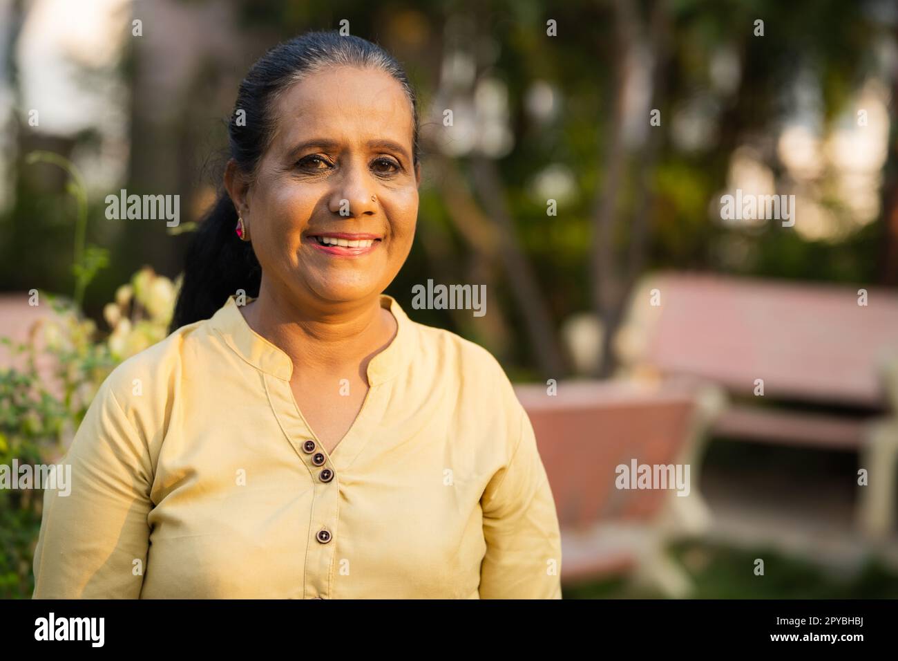 Felice donna anziana indiana sorridente in piedi guardando la macchina fotografica al parco - concetto di stile di vita di pensione, di successo e di relax Foto Stock