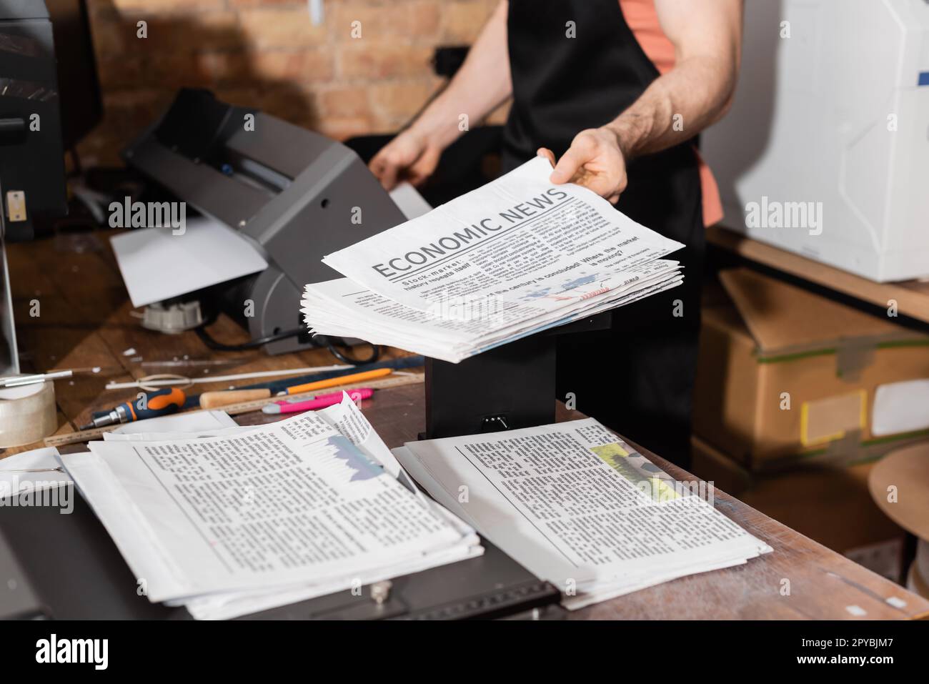 vista ritagliata del tipografo in grembiule che tiene giornali stampati con notizie economiche, immagine di riserva Foto Stock