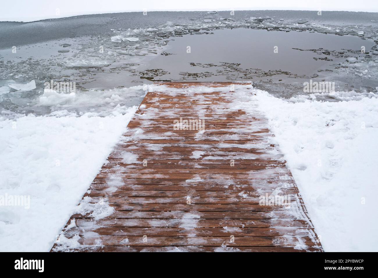 Luogo di nuoto sul ghiaccio con un sentiero in legno innevato che scende in acqua Foto Stock