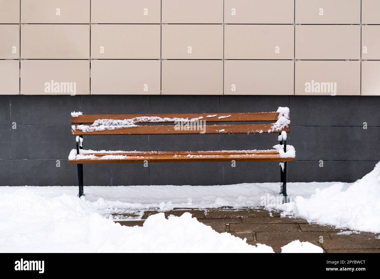 Panca in legno ricoperta di neve contro un muro dell'edificio Foto Stock