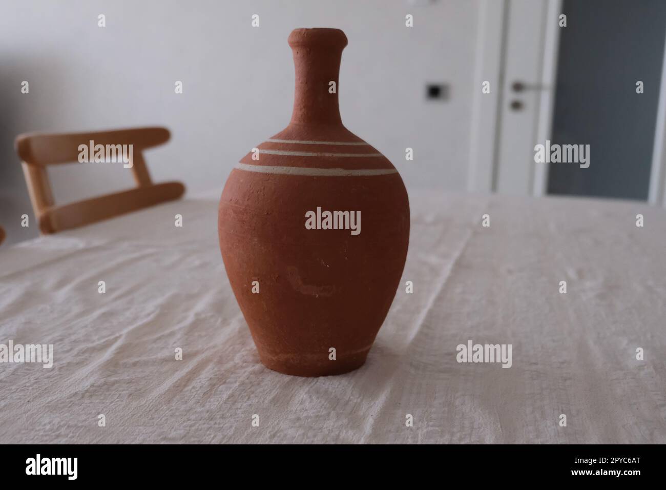 Vista frontale della vecchia caraffa in ceramica non dipinta su una tovaglia bianca. Caraffa di creta per bere vino o acqua. Foto Stock