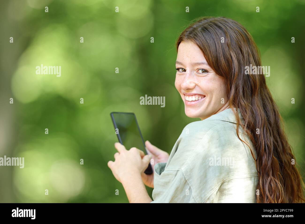 La donna felice ti guarda in un telefono nascosto in una foresta Foto Stock