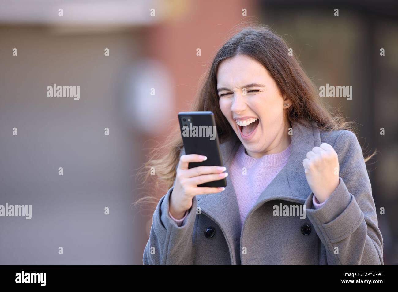 Donna eccitata che festeggia buone notizie tenendo il telefono in mano Foto Stock