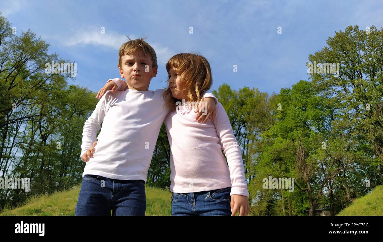 Ragazzo e ragazza in posa. Abiti alla moda. Camicia o blusa a maniche lunghe bianca, jeans e pantaloni blu. Sullo sfondo c'è il verde degli alberi. Ragazza che guarda il ragazzo Foto Stock