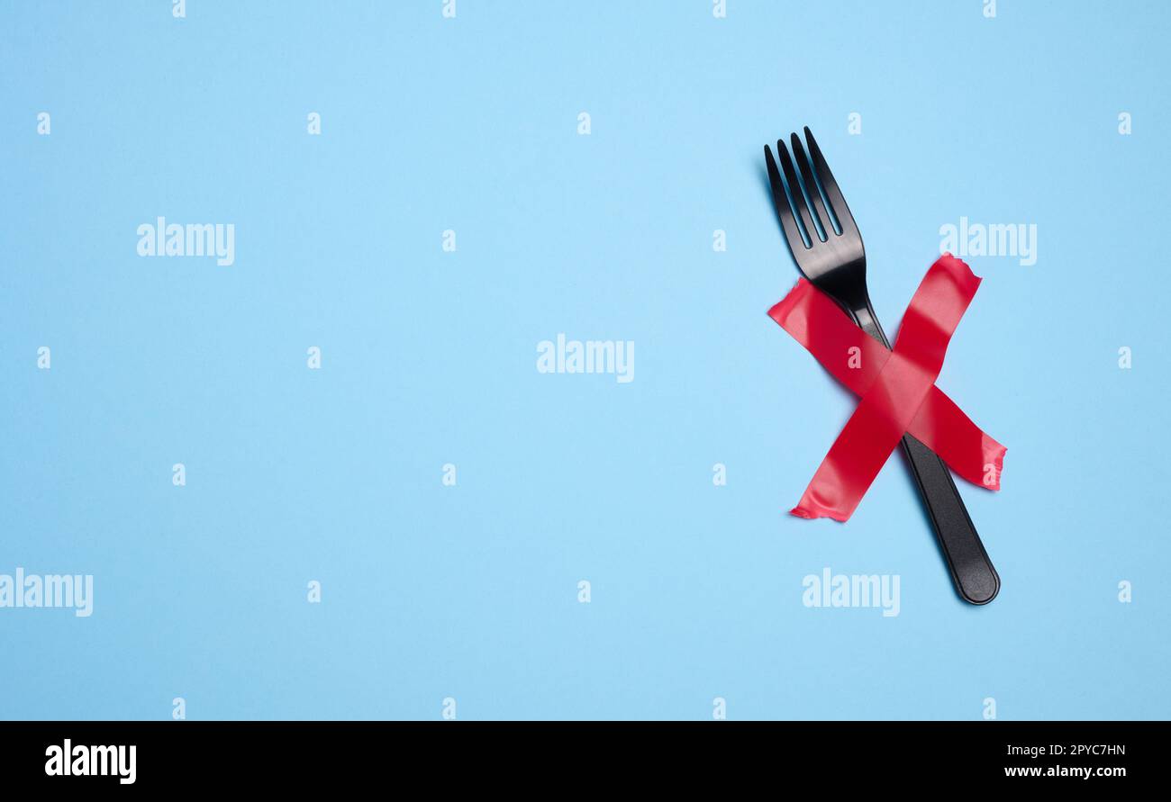 Una forchetta in plastica è fissata con nastro adesivo rosso su sfondo blu, un concetto di rifiuto di stoviglie in plastica e materiali di riciclaggio, zero rifiuti Foto Stock