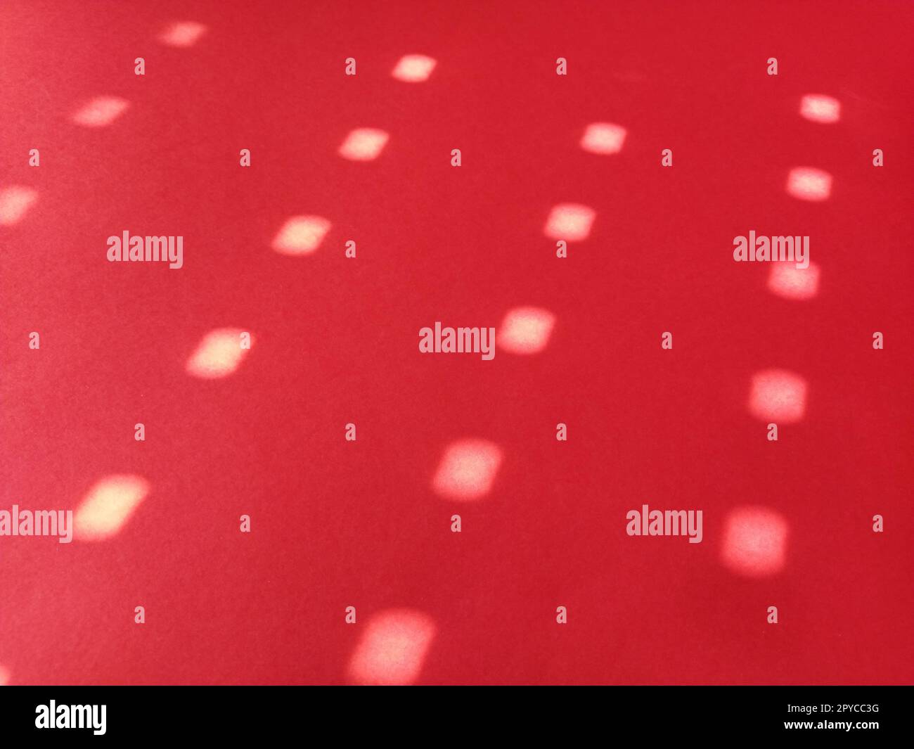 Sfondo rosso con pois. Raggi del sole che brillano attraverso i fori nelle tende e dipingono cerchi chiari e sfocati sulla superficie colorata Foto Stock