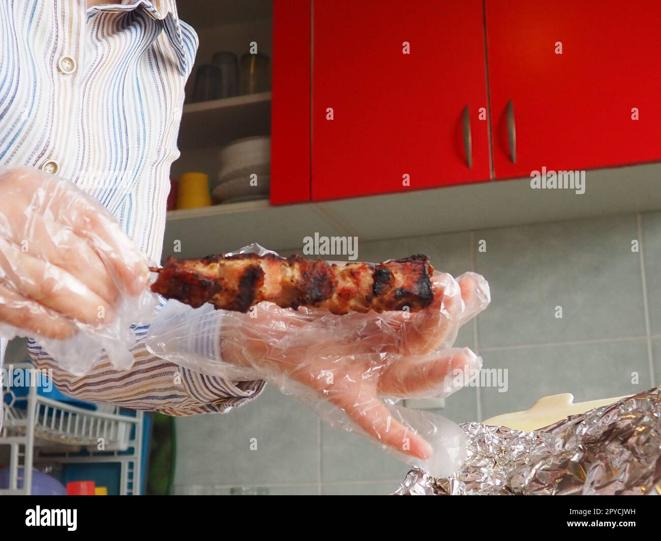 Carne alla griglia in confezioni usa e getta e foglio di alluminio del ristorante. Consegna a domicilio da ristoranti e caffetterie. Le mani femminili nei guanti usa e getta tengono la carne su un bastoncino. Foto Stock