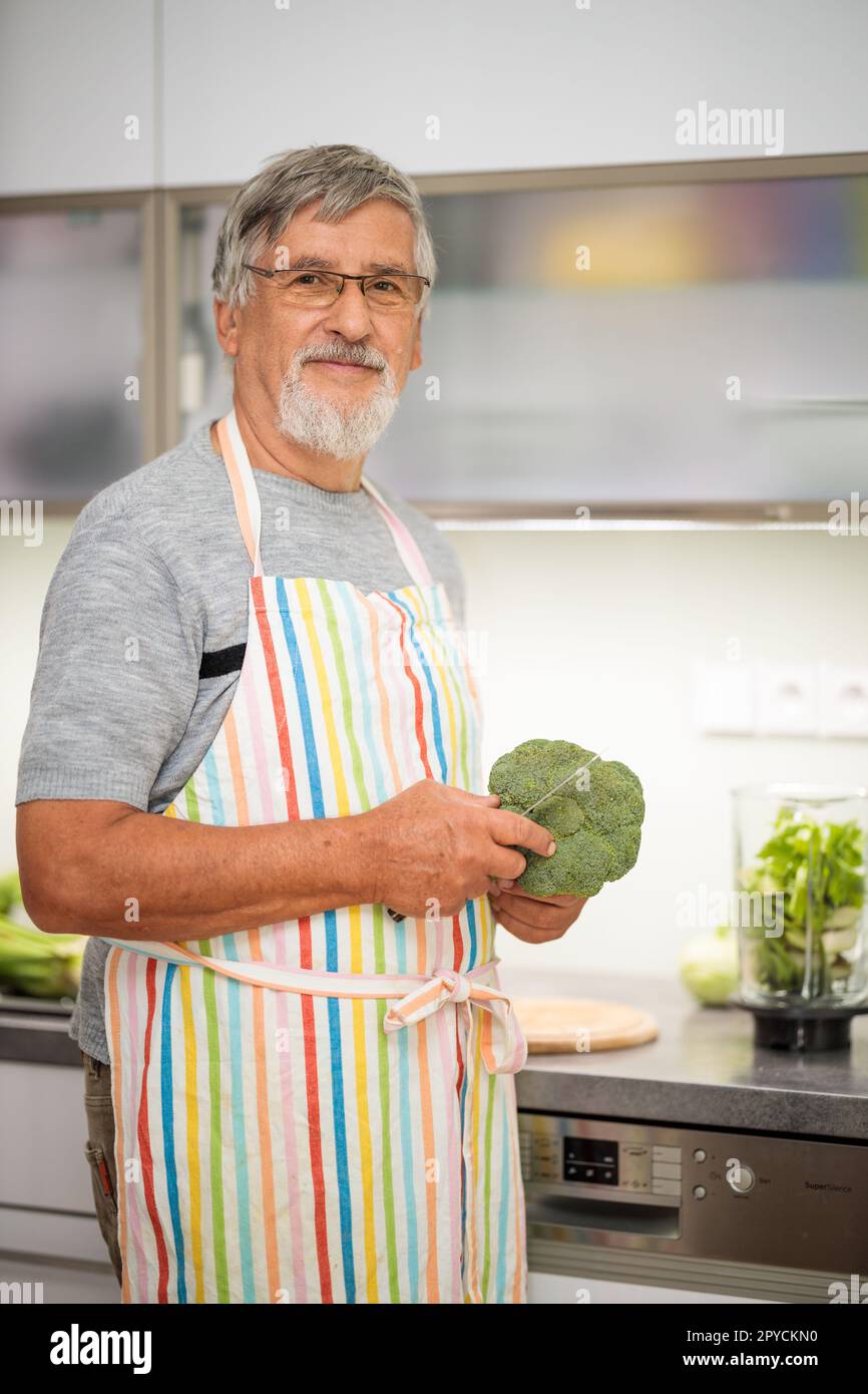 Uomo anziano che prepara i broccoli, taglia i broccoli nella cucina di casa, prepara un piatto sano pieno di nutrienti. Foto Stock