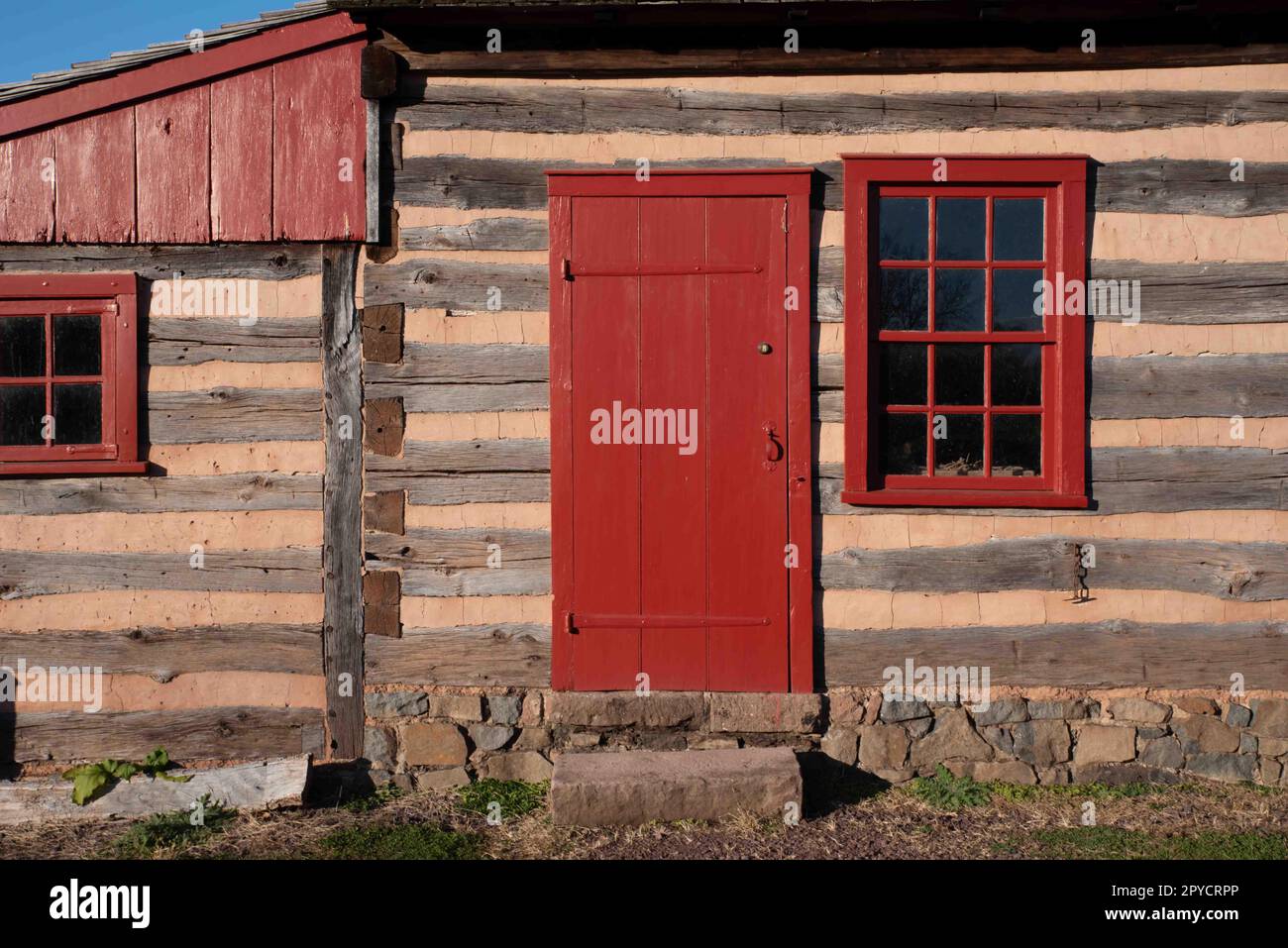 Esterno della cabina in legno coloniale con finestra e porta rosse Foto Stock