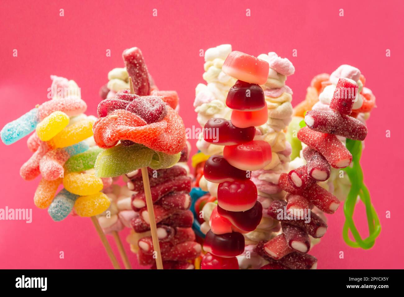 Variazione di frutta colorata gomme dolci spiedini orsetti di gommosa acidata su spiedini di legno isolati su uno sfondo rosso magenta Foto Stock