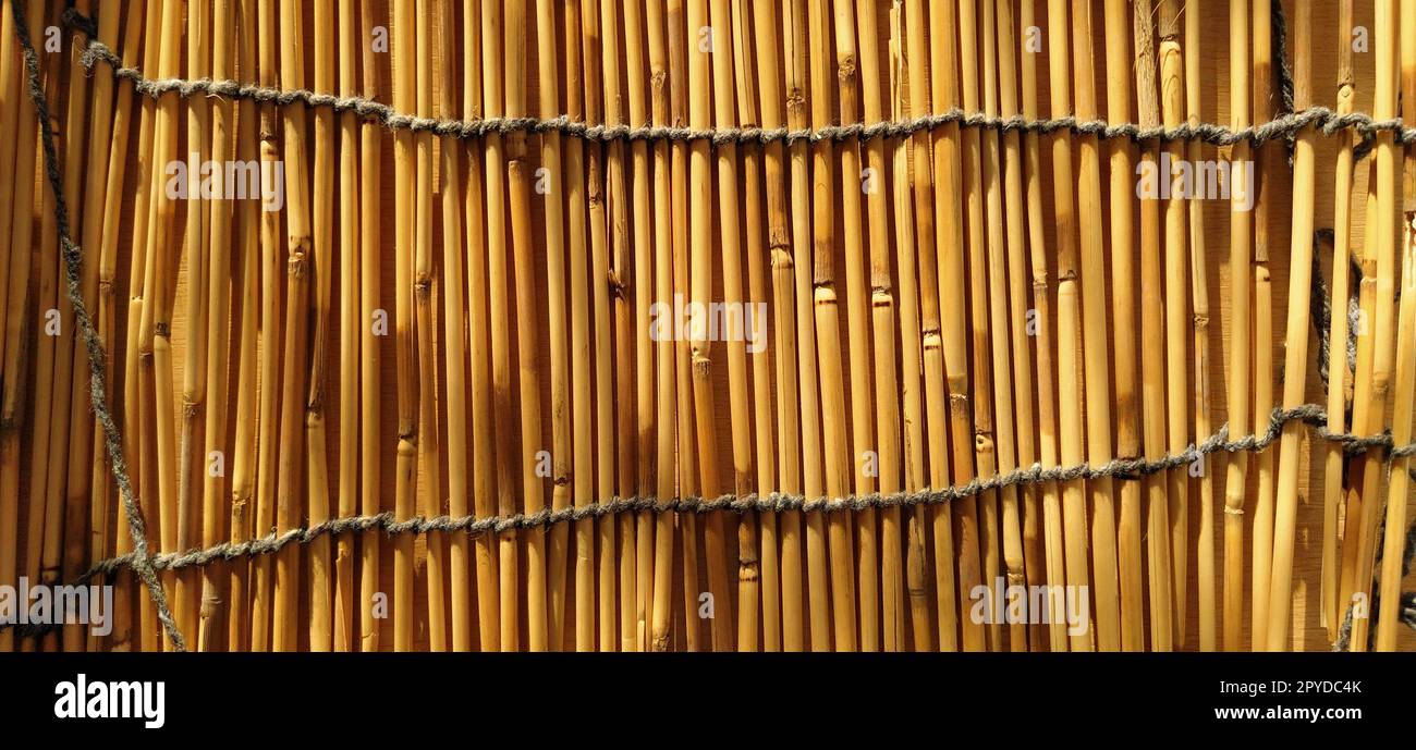 Una biancheria da letto in paglia, una tovaglia o un piccolo tappeto appoggiato su un tavolo e fotografato lateralmente. La luce del sole della sera si riflette sui gambi. Alcuni bastoncini sono rotti, fili e funi sono intrecciati Foto Stock