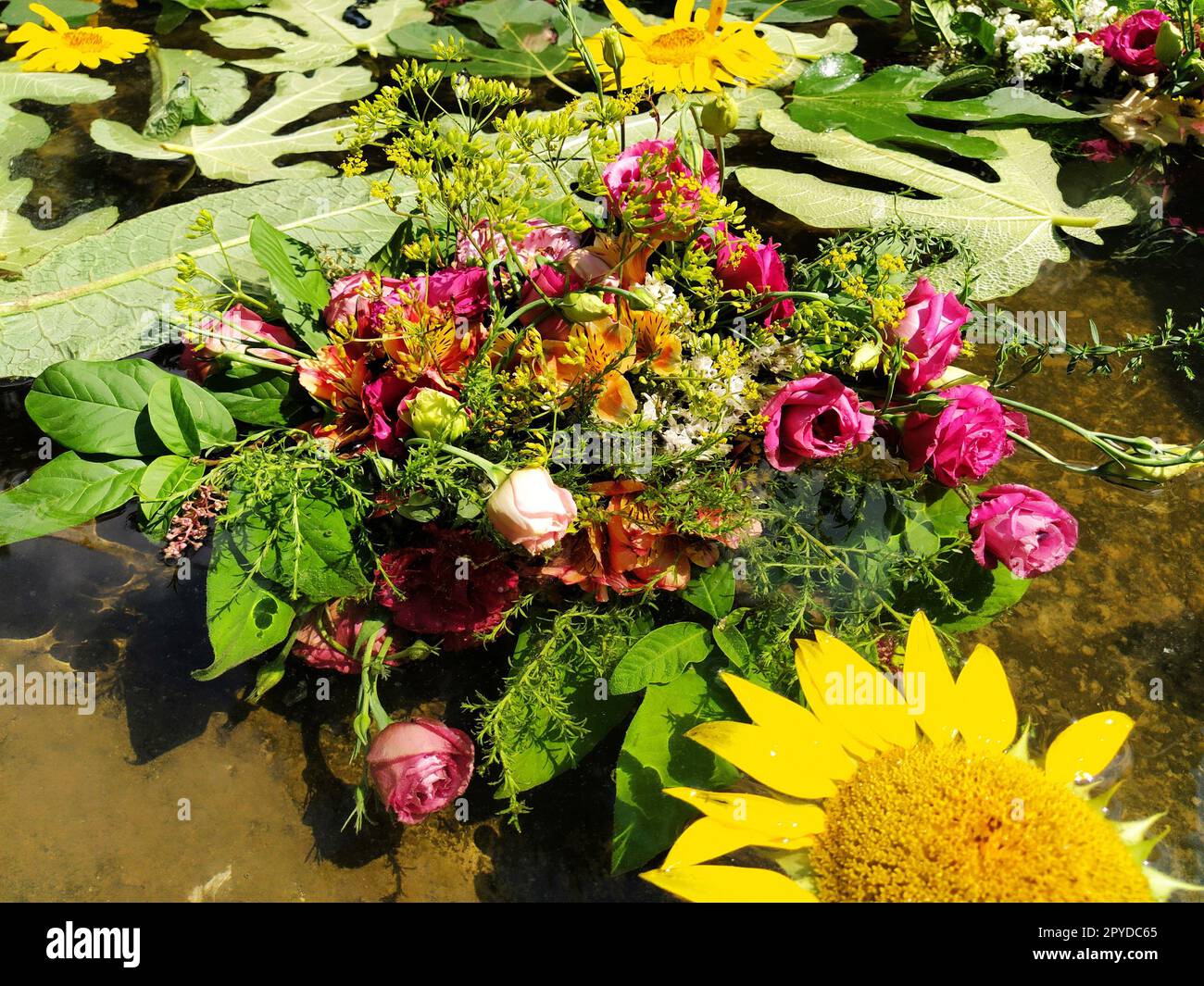 Girasoli decorativi gialli, rose rosa e rosse in un bouquet galleggiante nell'acqua di uno stagno. Boccioli a pizzico come decorazione per una vacanza estiva. Ivan Kupala, solstizio d'estate. Festival del raccolto. Foto Stock