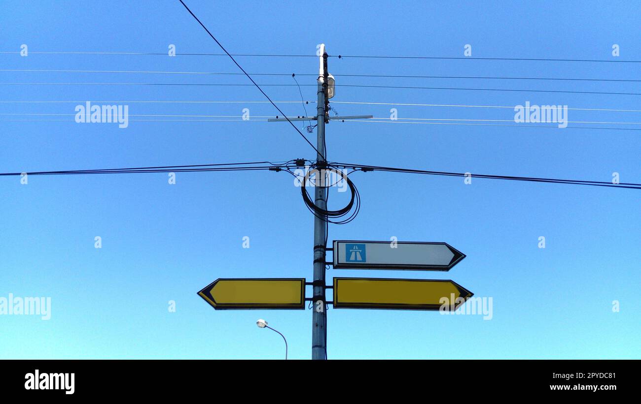 Indicatore di direzione bianco vuoto rivolto a destra. indicazioni stradali. Le frecce gialle e bianche sono segnalate sulla strada o all'incrocio. cielo blu sullo sfondo. Fili elettrici avvolti in circolo. Foto Stock