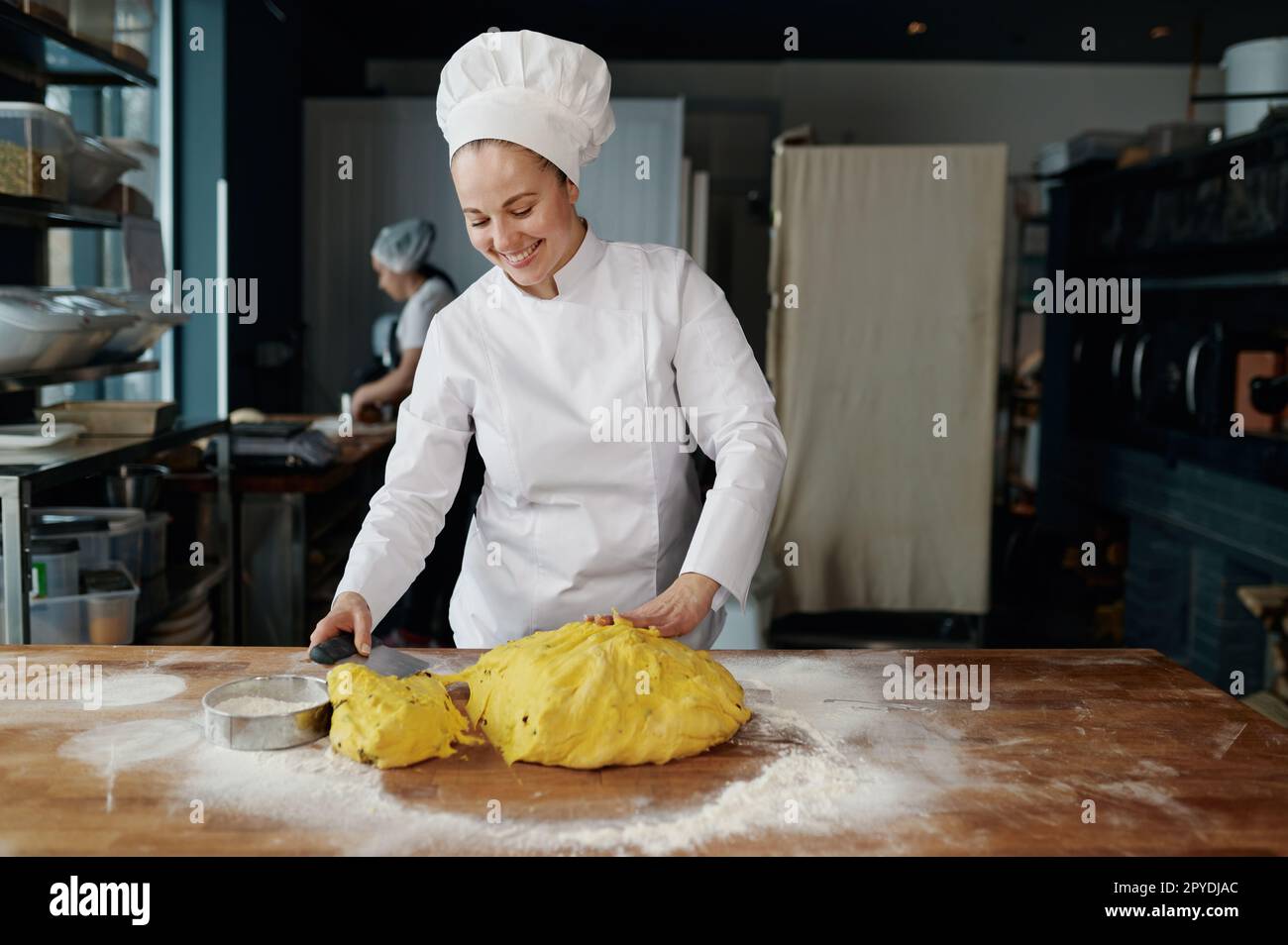 Felice donna sorridente fornaio pezzo di pasta tagliata con coltello su tavolo di legno Foto Stock