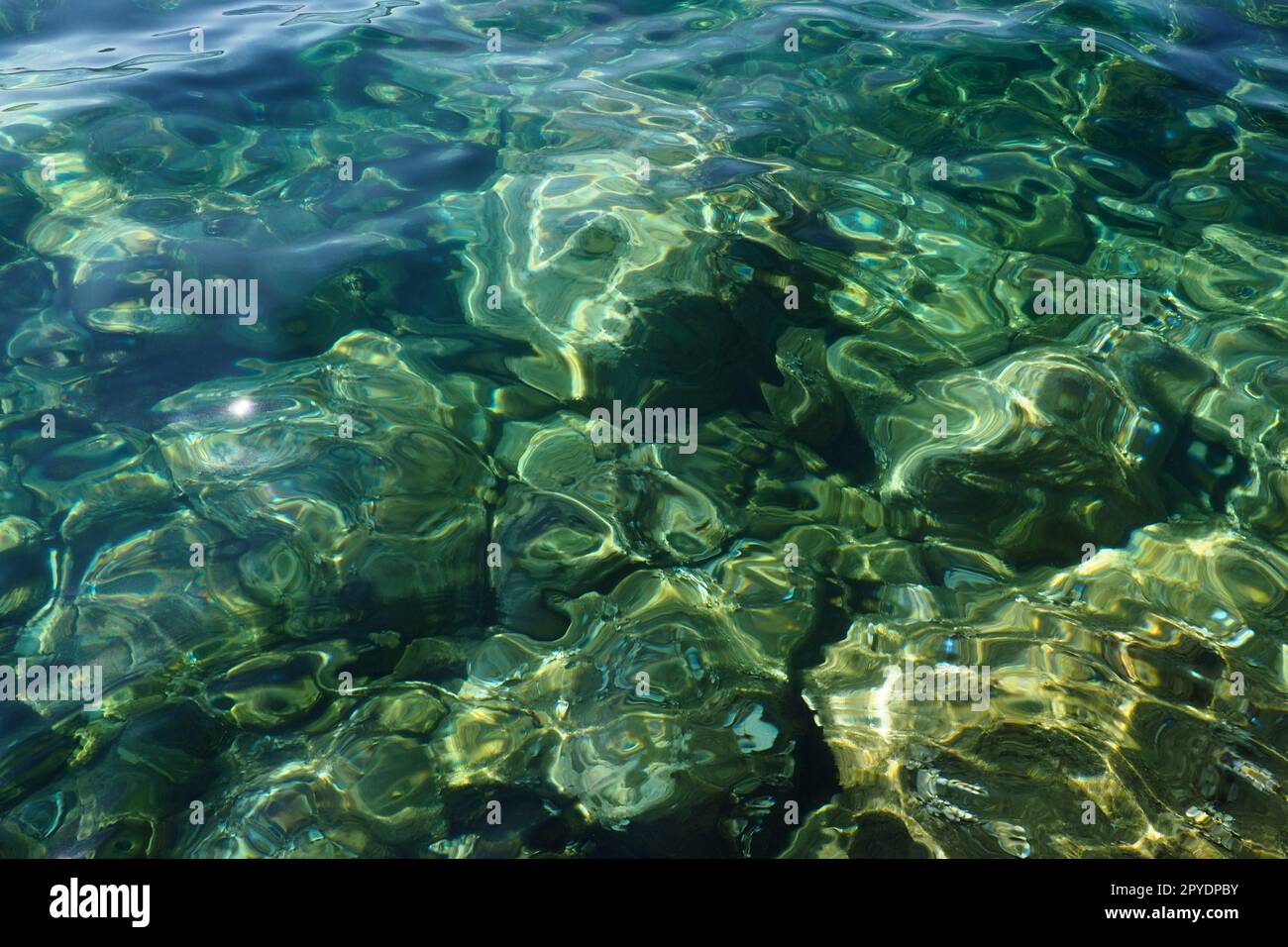 Consistenza di acqua salata trasparente blu turchese verde. Vista dall'alto della superficie dell'acqua e delle increspature. Acqua onde di mare sullo sfondo. Il fondo roccioso con alghe è visibile attraverso l'acqua cristallina Foto Stock