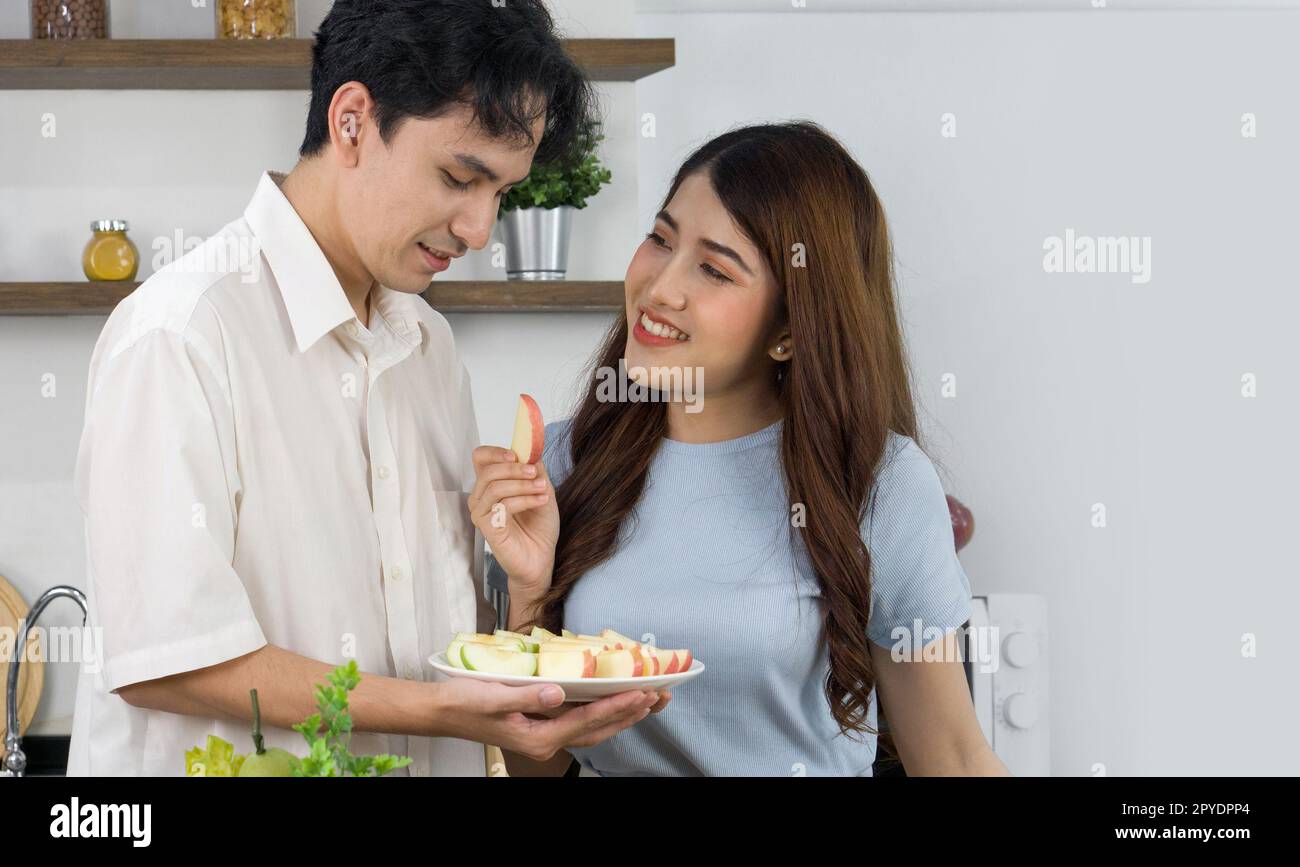 Coppie asiatiche trascorrono del tempo insieme in cucina. Giovane donna nutrire il suo ragazzo un pezzo di mela. Foto Stock