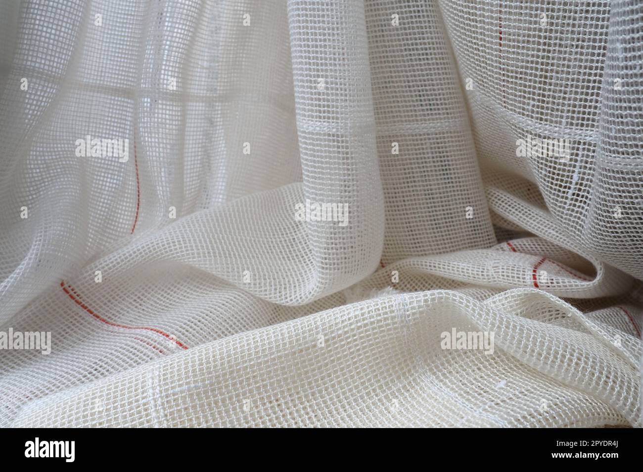 Tende bianche in cotone grossolano o lino fatte di trame di fili sottili. Appartamento interno semplice, compatto ed economico. Decorazione delle finestre in camera. Striscia rossa. Foto Stock