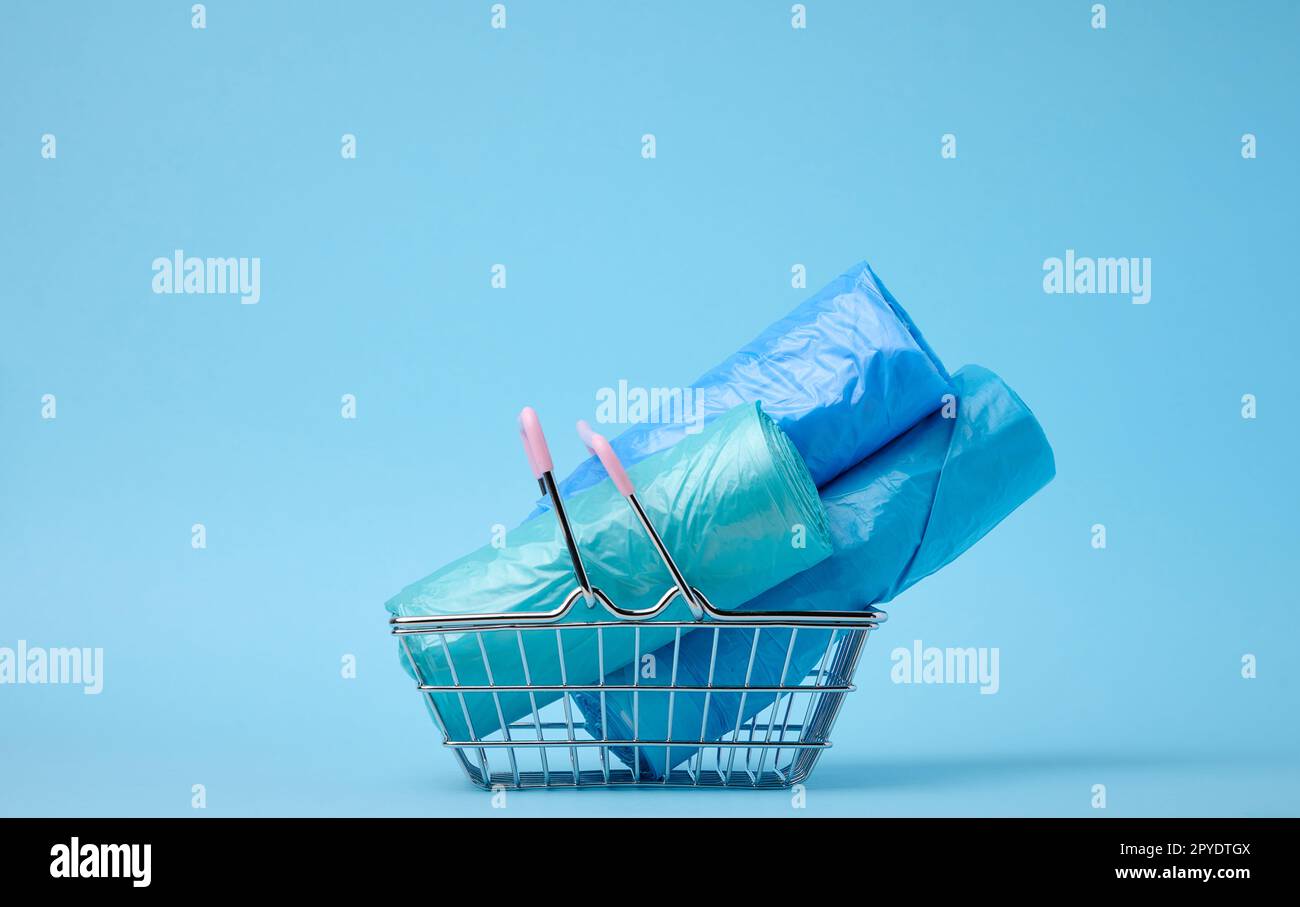 Rotoli di sacchetti di plastica in un cestino della spesa in miniatura su uno sfondo blu Foto Stock