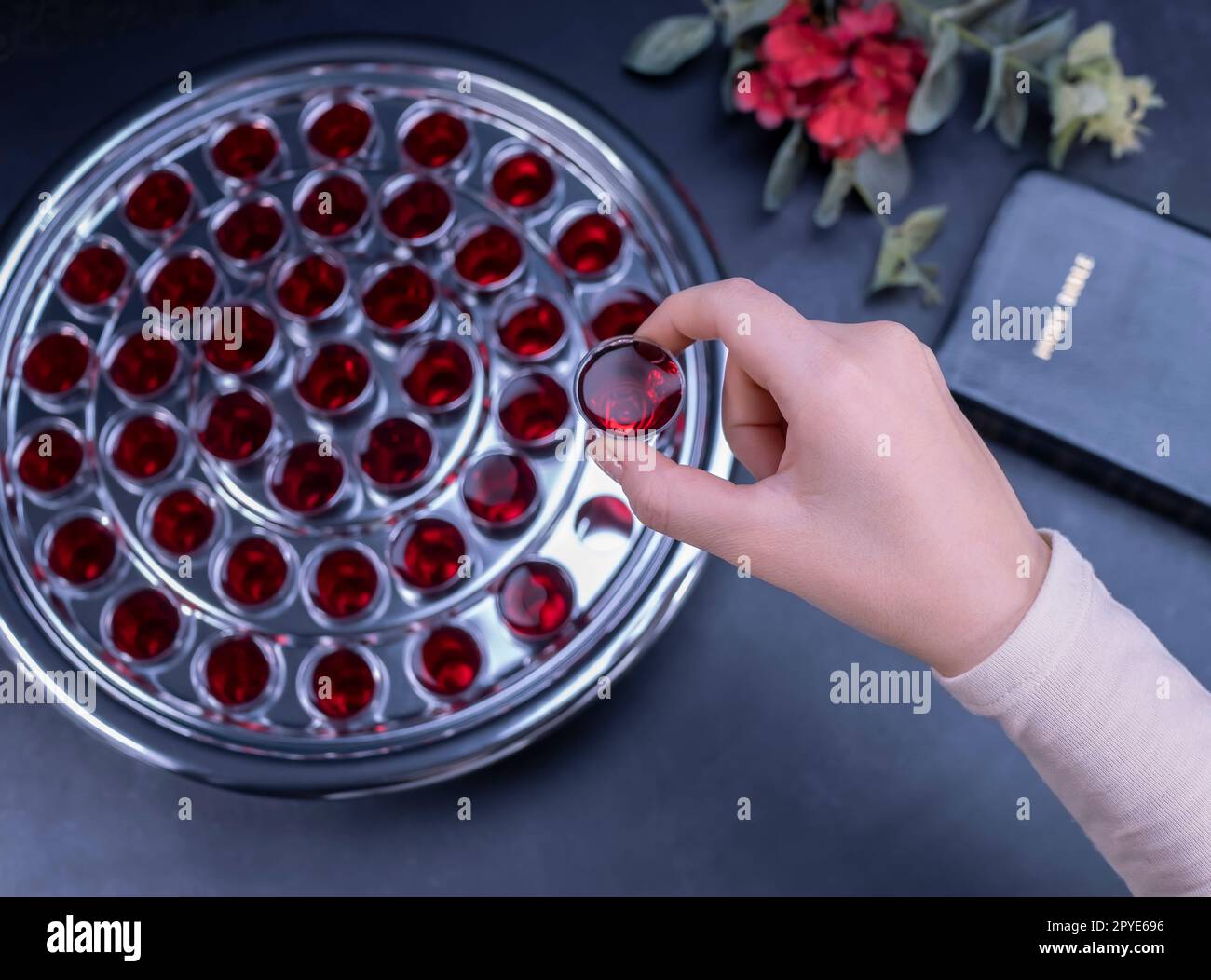 Primo piano di una giovane donna che prende la comunione da piccole tazze su sfondo nero Foto Stock