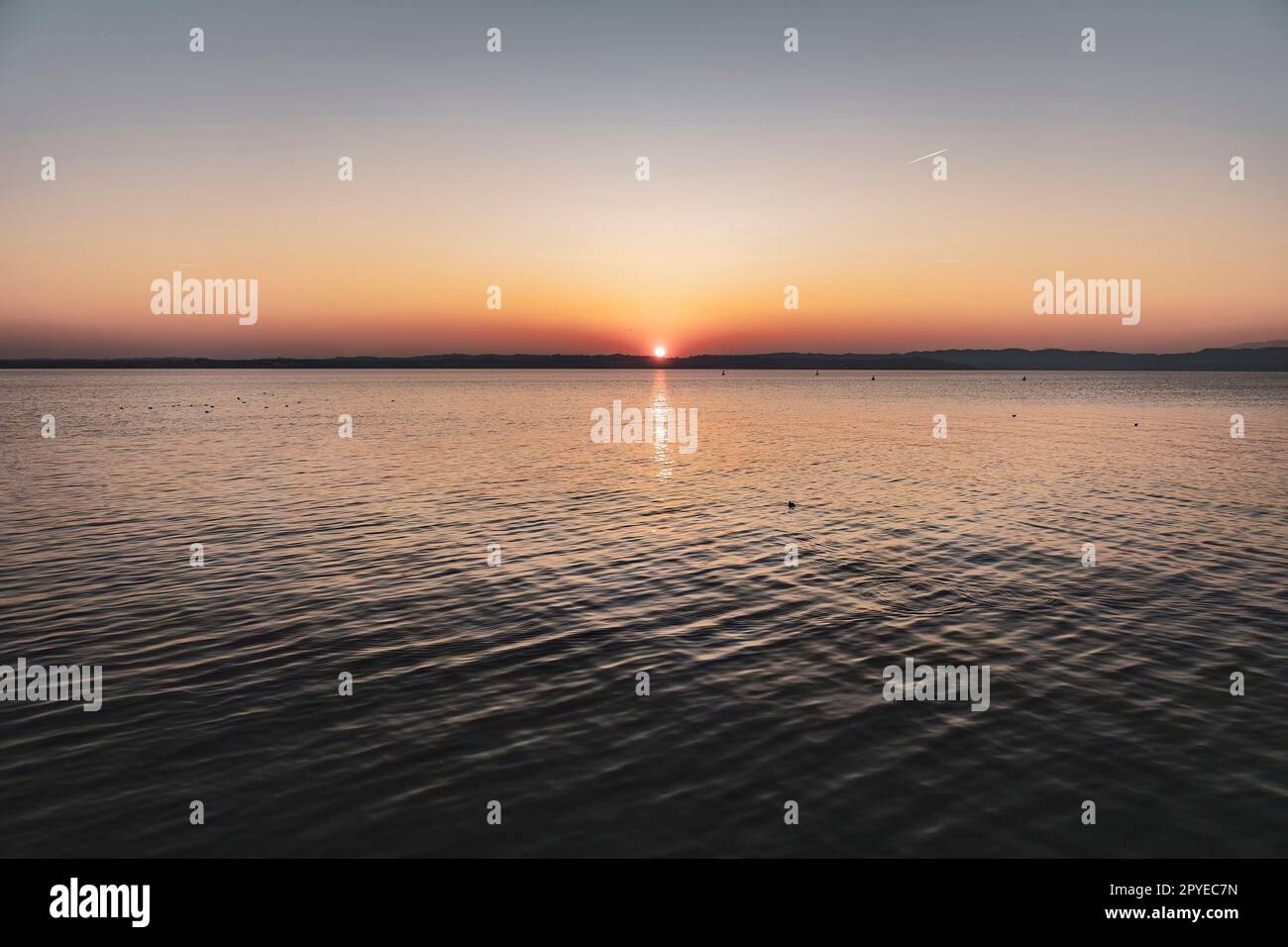 Splendido tramonto sullo splendido lago di Garda in Italia, con il sole che si riflette sulle acque calme Foto Stock