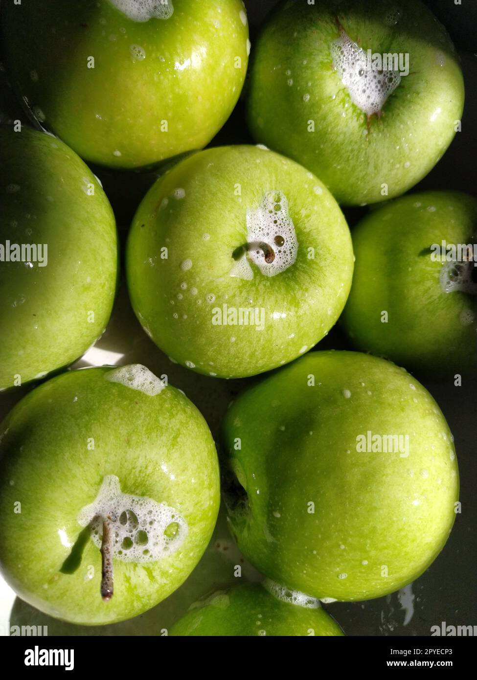 Mele verdi e sapone umide. Lavare accuratamente verdure e frutta con acqua e sapone. Prevenzione di malattie infettive. Primo piano delle mele. Vegetarianismo. La schiuma saponata splende alla luce del sole Foto Stock