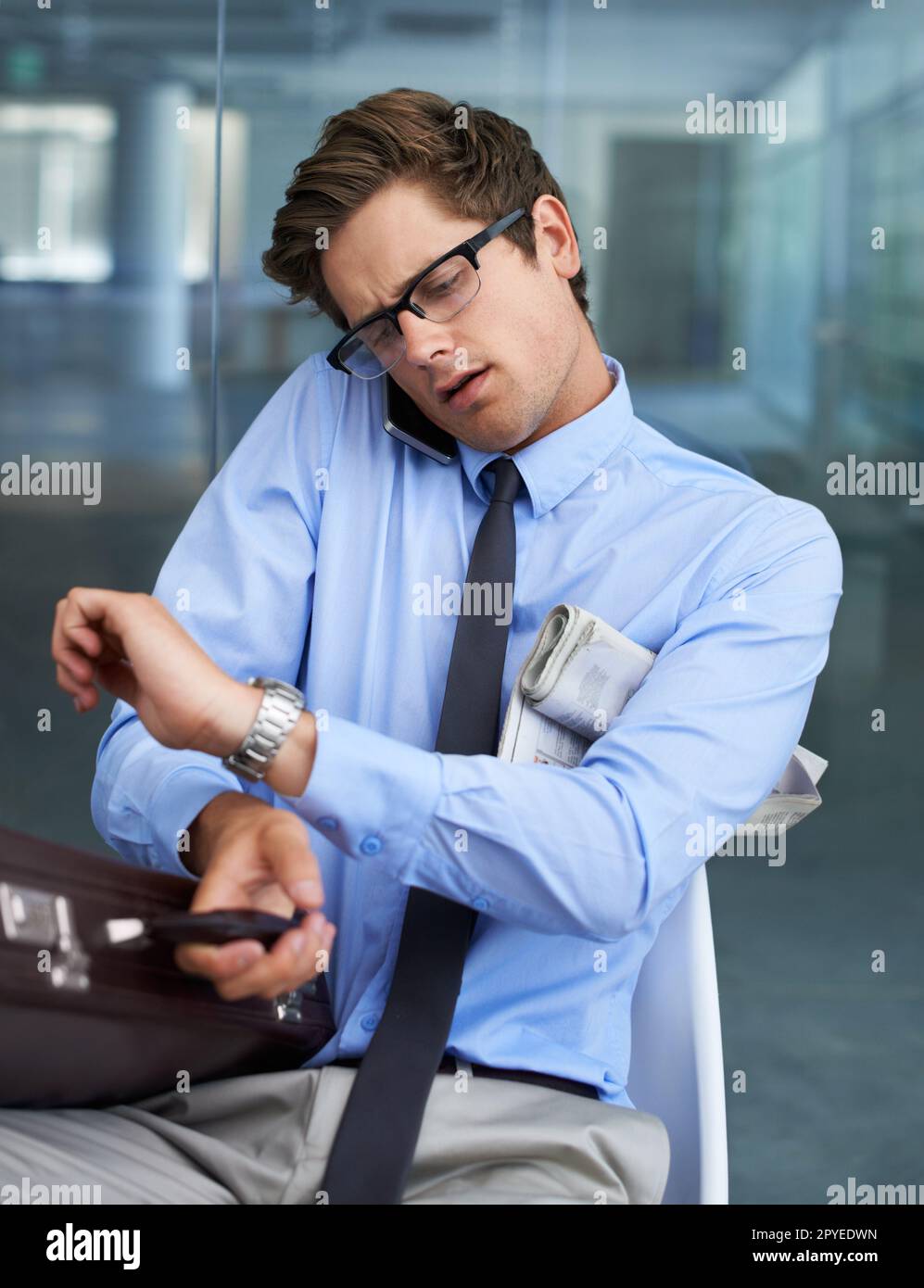 La gestione del tempo è difficile. Un giovane imprenditore impegnato che controlla il tempo mentre prende una chiamata. Foto Stock