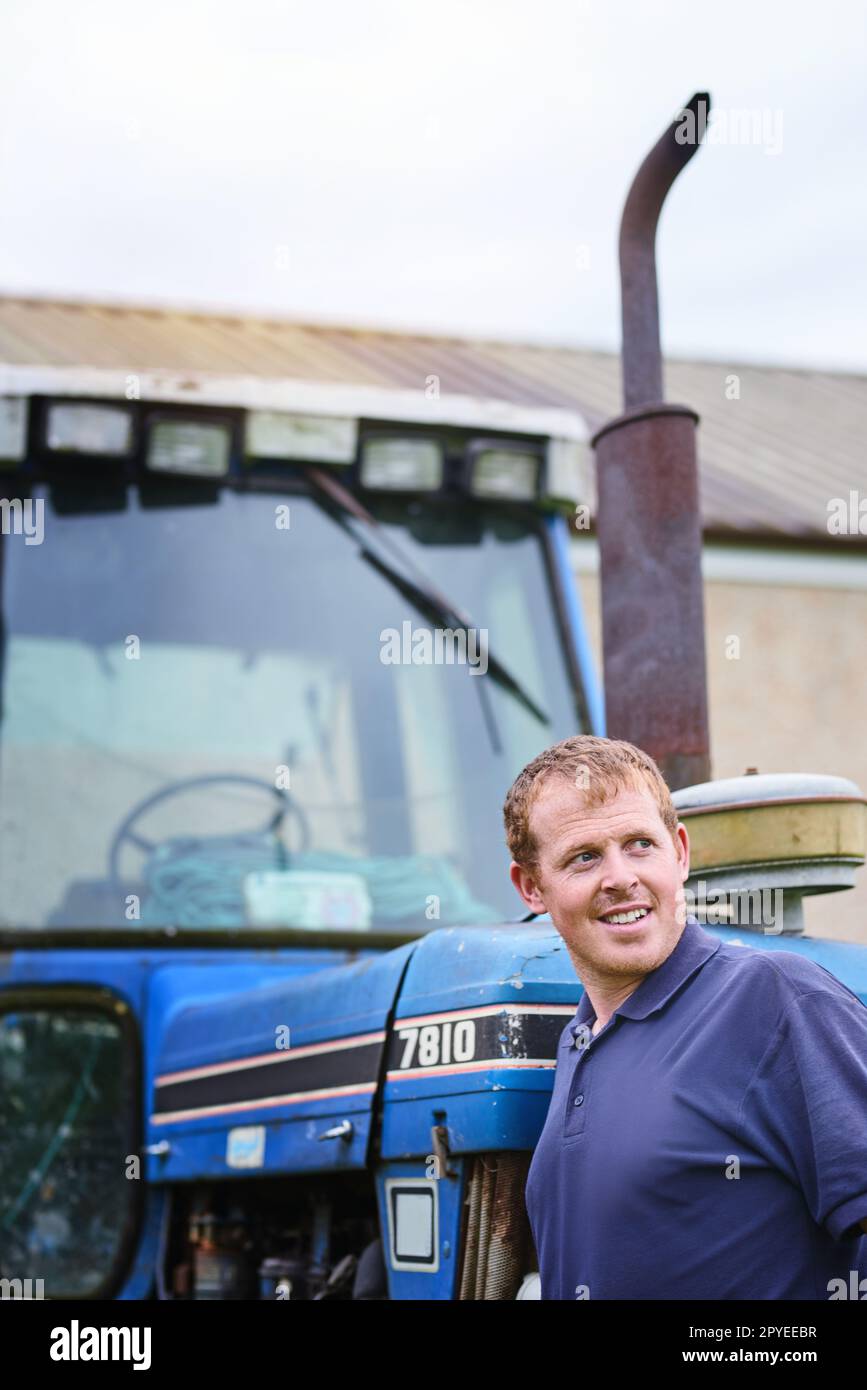 Pensato per essere il migliore del settore agricolo. un agricoltore che si trova accanto a un trattore in un'azienda agricola. Foto Stock