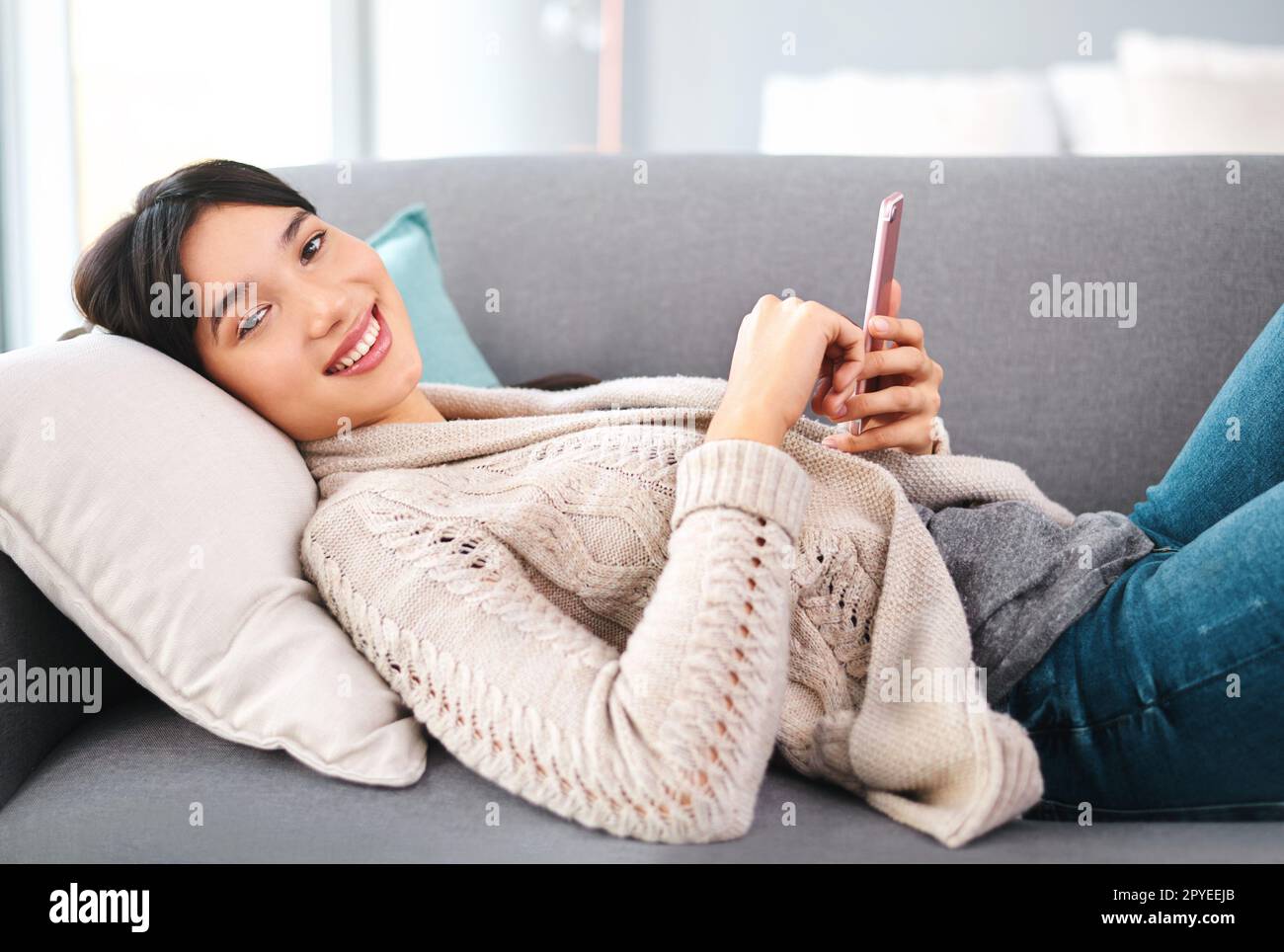 Fare ciò che noi giovani facciamo meglio. Ritratto di una giovane donna allegra che naviga sul cellulare mentre si rilassa su un divano a casa durante il giorno. Foto Stock