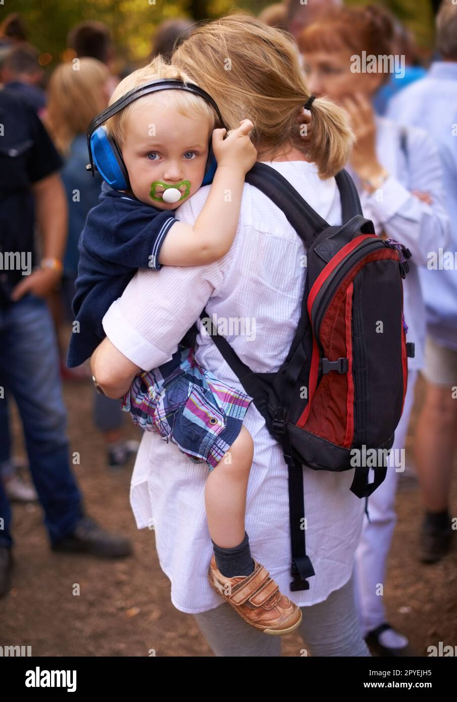 Proteggere le sue orecchie sensibili al festival. un bambino che è portato da sua madre ad un festival all'aperto. Foto Stock