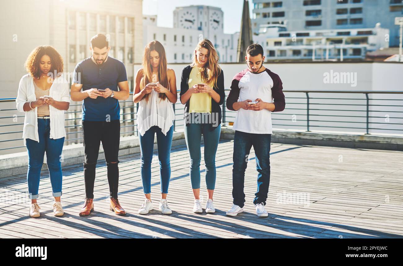 Questa è la nuova vita sociale. Foto a tutta lunghezza di un gruppo di giovani che testano sul proprio cellulare mentre si è in piedi all'aperto. Foto Stock