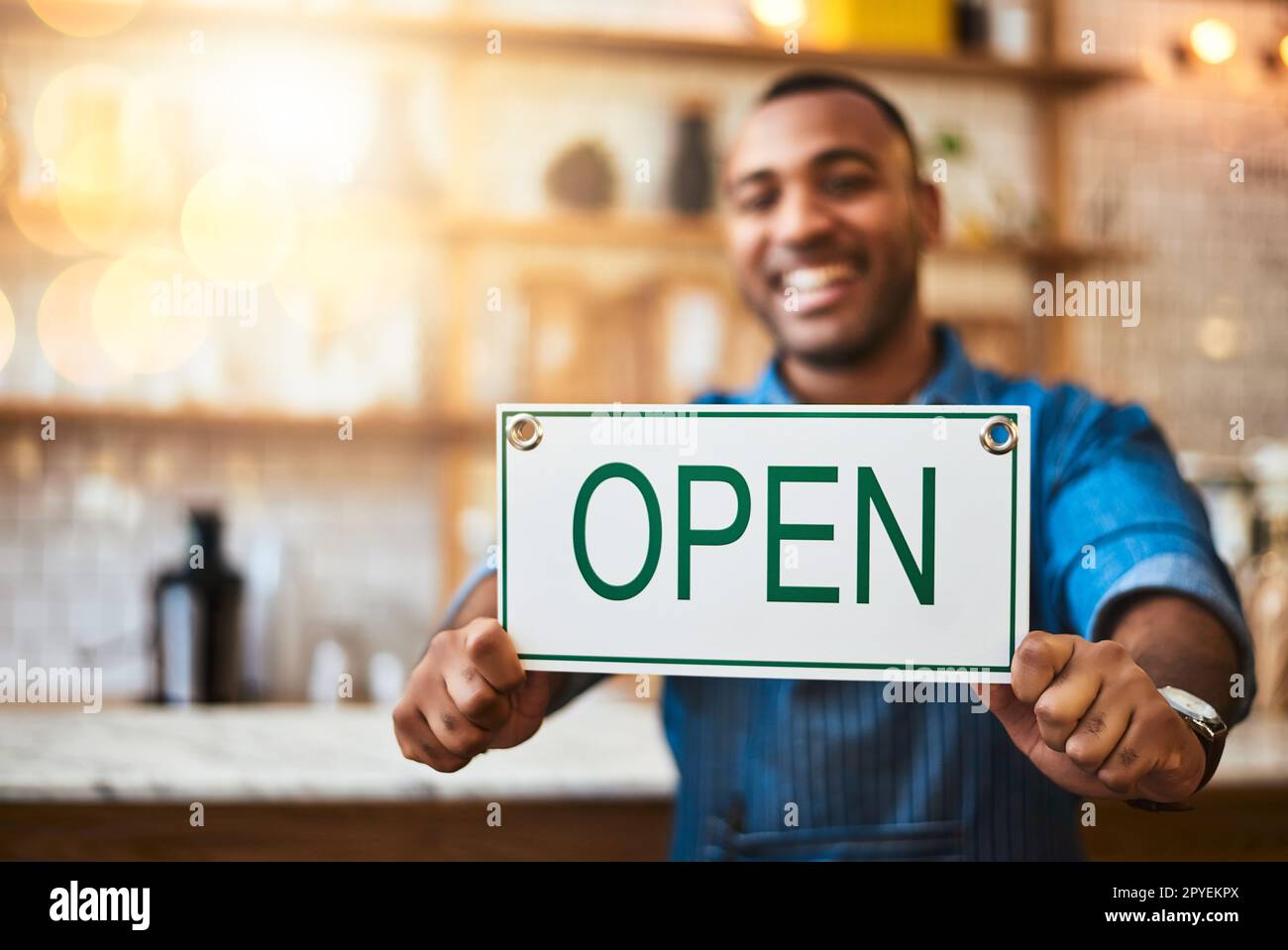 Perché non sostenere il vostro caffè locale per un cambiamento. Ritratto di un giovane uomo che tiene un segno aperto nel suo negozio. Foto Stock