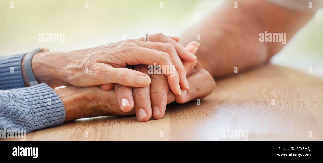 Senior, tenendosi per mano e supportando la coppia, il comfort e l'aiuto sul tavolo per il dolore, il dolore o la simpatia. Uomo anziano, anziano e aiutante per empatia, amore e cura a casa con il legame Foto Stock