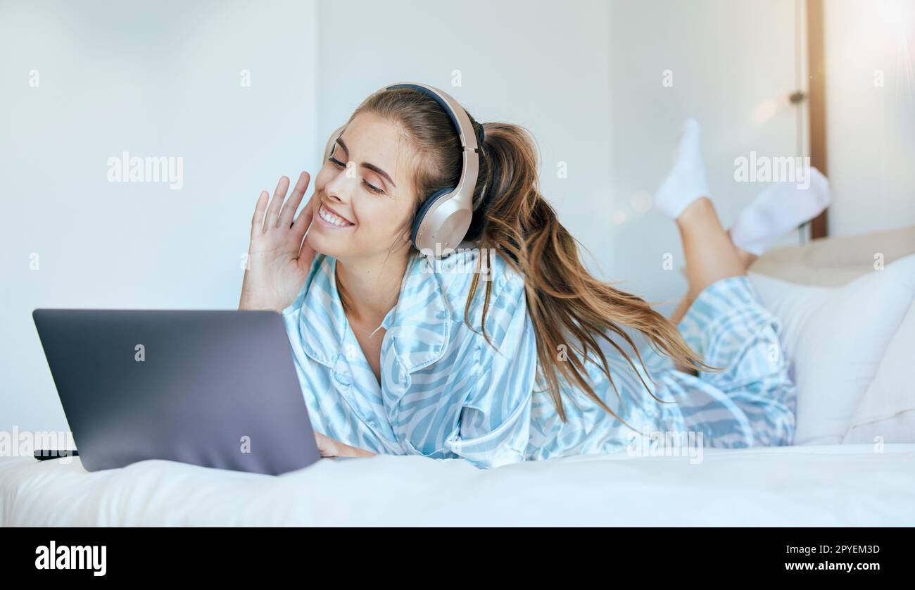 Donna, cuffie e relax sul laptop in camera da letto per scaricare film, programmi online e intrattenimento multimediale a casa. Felice giovane donna, musica e computer per abbonamento streaming, podcast e audio Foto Stock