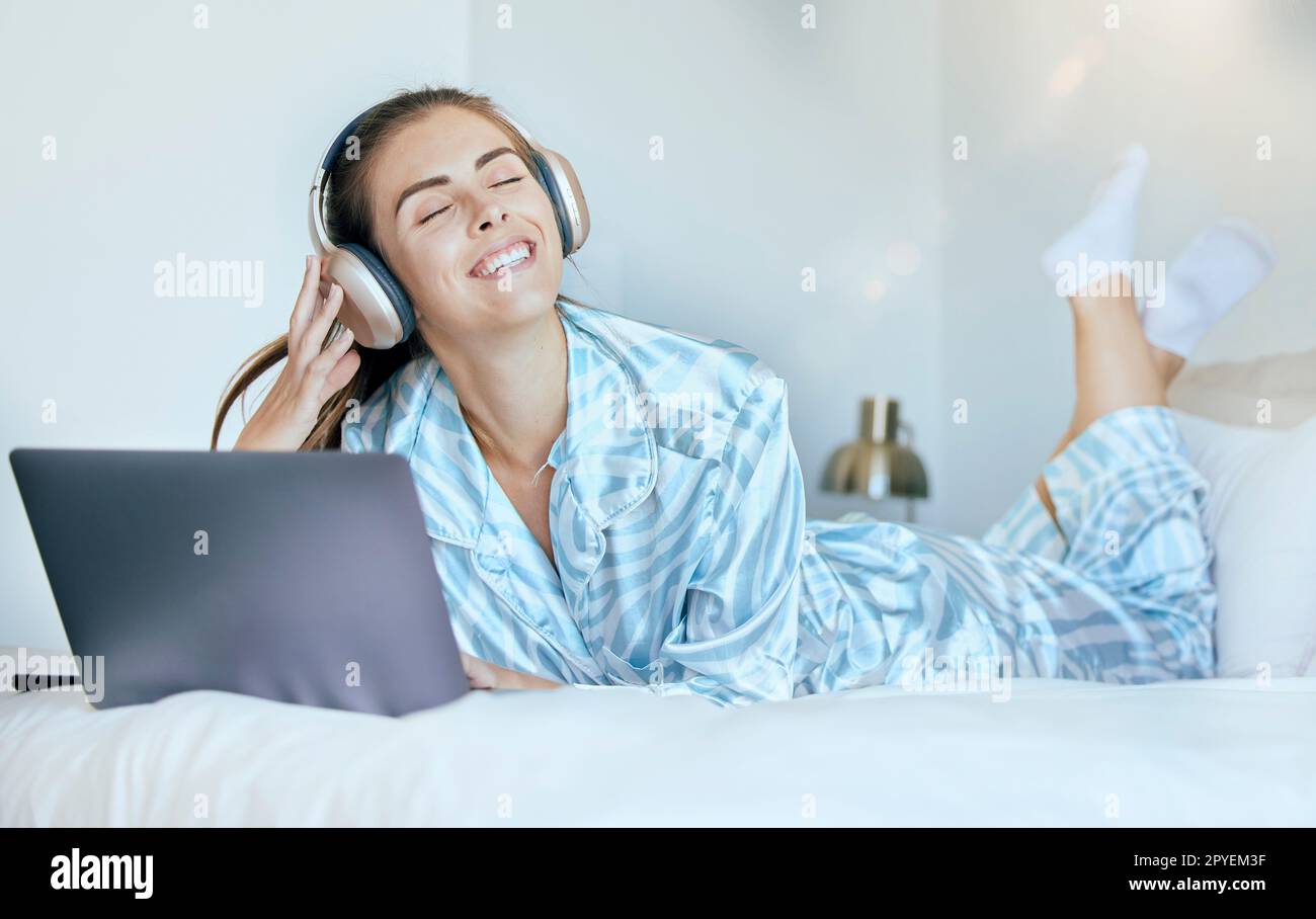 Cuffie, computer portatile e donna sul letto con musica per la salute mentale, relax e benessere al sole del mattino o luce parassita dell'obiettivo. Donna felice o studente su Internet, abbonamento streaming audio in camera da letto Foto Stock