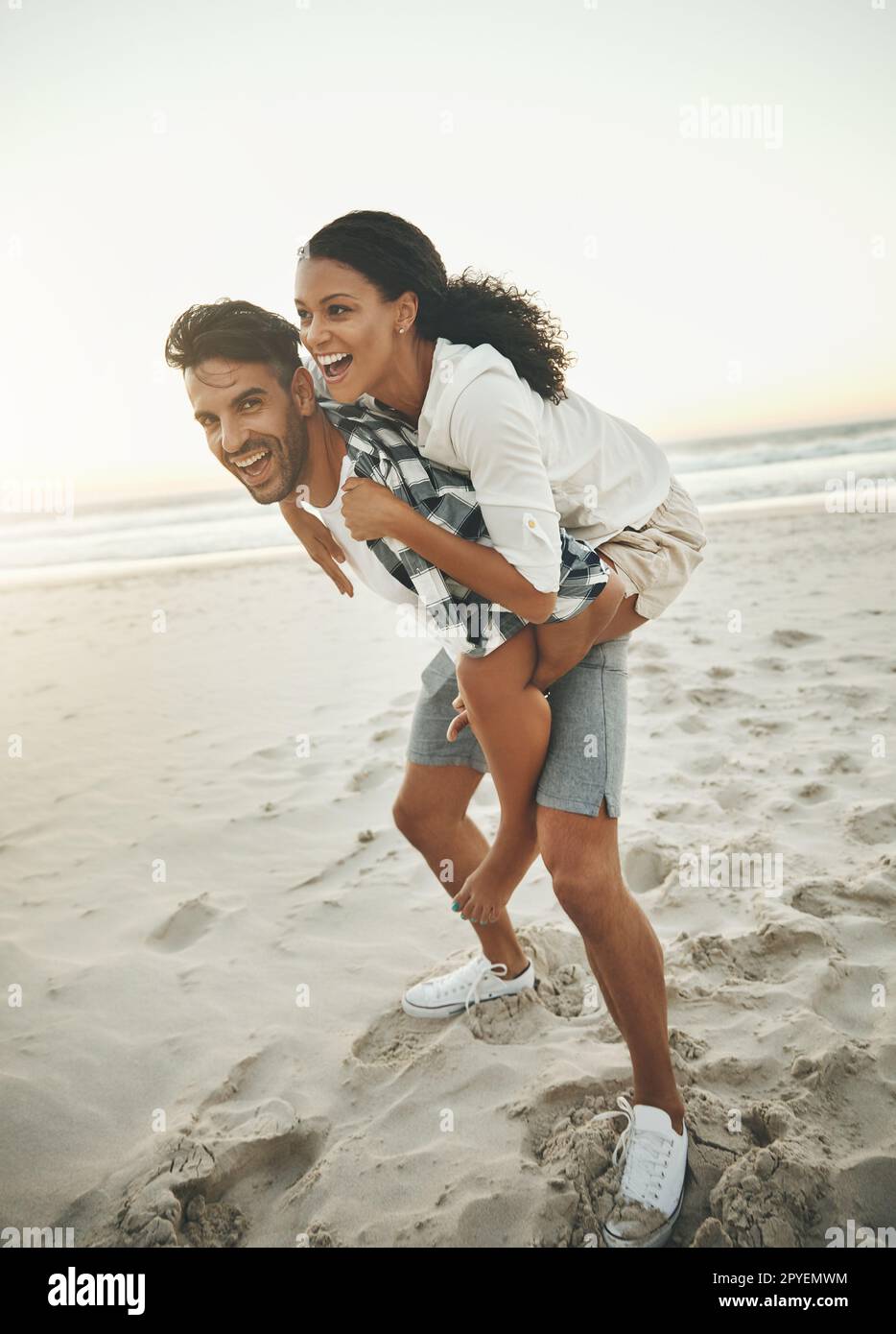 L'amore fa girare il mondo. un giovane piggybacking della sua ragazza mentre passa la giornata in spiaggia. Foto Stock